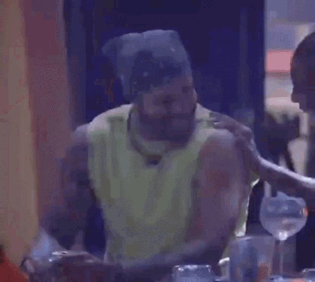 a man in a green tank top is sitting at a table with a tray of food .