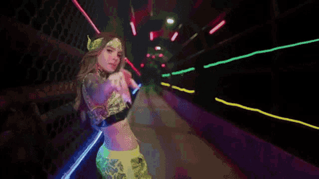 a woman in a neon outfit is dancing in a tunnel with neon lights .