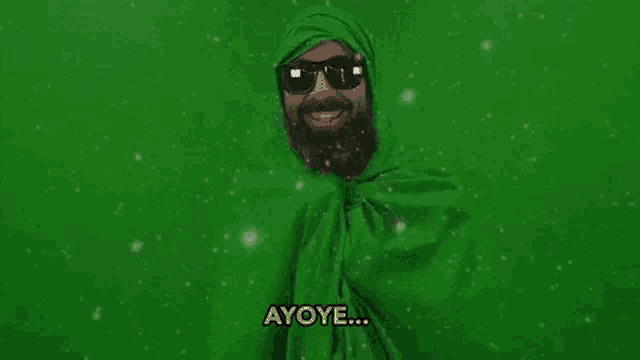 a man with a beard and sunglasses is wrapped in a green cloth and smiling .