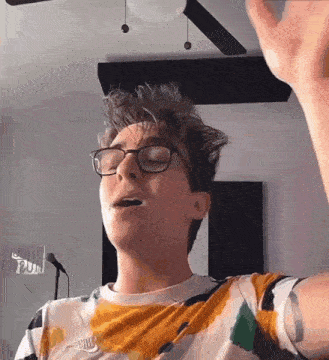 a young man wearing glasses is singing into a microphone .