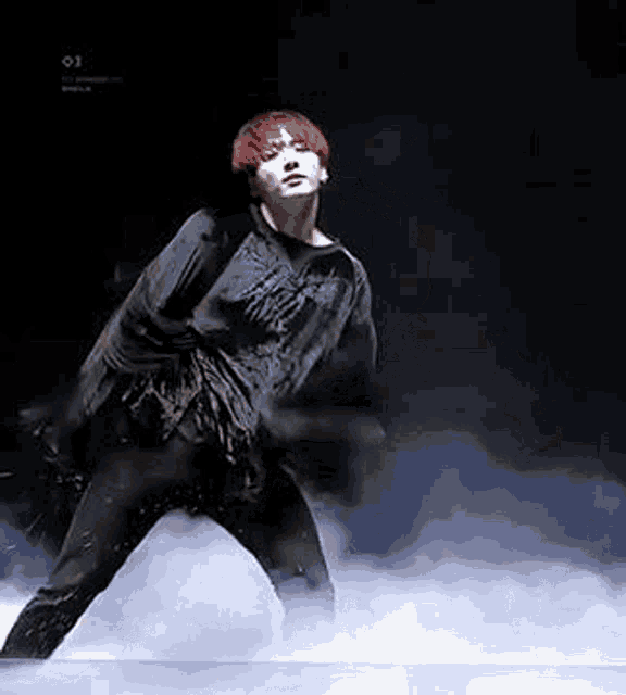 a man with red hair is dancing on a stage with smoke coming out of it .