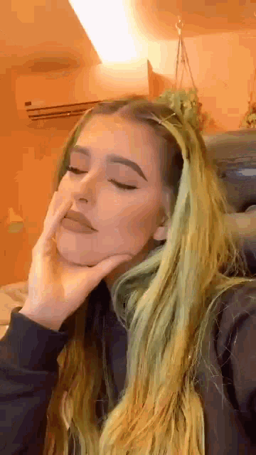 a woman with long blonde hair is taking a selfie with her hand to her face .