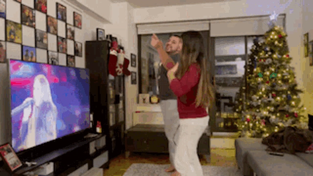 a man and a woman are dancing in front of a christmas tree in a living room