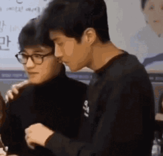 two young men are standing next to each other and one of them has glasses on .