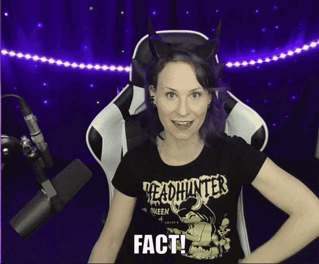 a woman wearing a headhunter queen t-shirt is sitting in front of a microphone