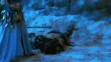 a woman in a blue dress is standing next to a man in a blue dress laying on the ground .