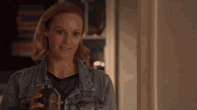 a woman in a denim jacket is holding a bottle