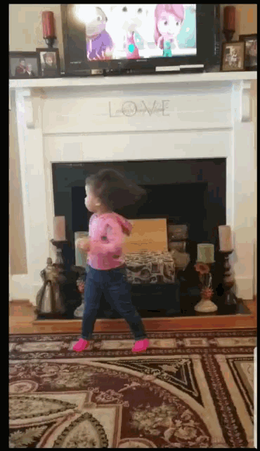 a little girl dancing in front of a fireplace with the word love written on it