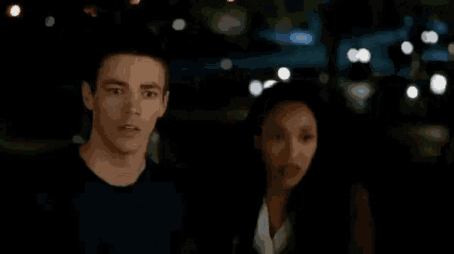 a man and a woman are standing next to each other in the dark . the man is wearing a ring on his finger .