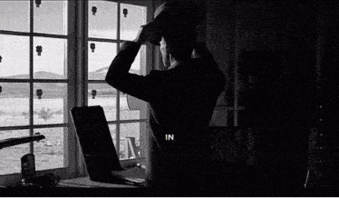 a black and white photo of a man standing in front of a window with the word in on the bottom