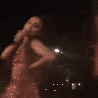 a blurry picture of a woman in a pink dress singing into a microphone