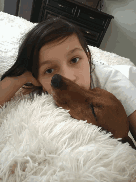 a young girl laying on a bed with a brown dog
