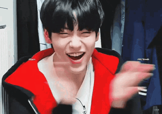 a young man wearing a red jacket and a white shirt is laughing