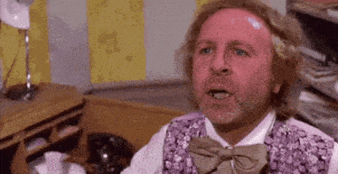 a man with a beard is wearing a purple vest and bow tie and making a funny face .