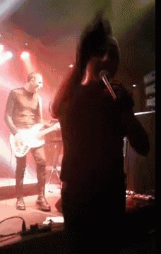 a man singing into a microphone while another man plays a guitar on stage