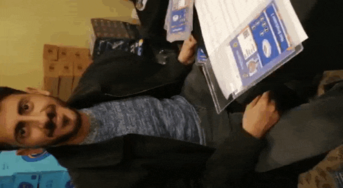 a man with a beard is sitting on the floor holding a piece of paper in his hands .