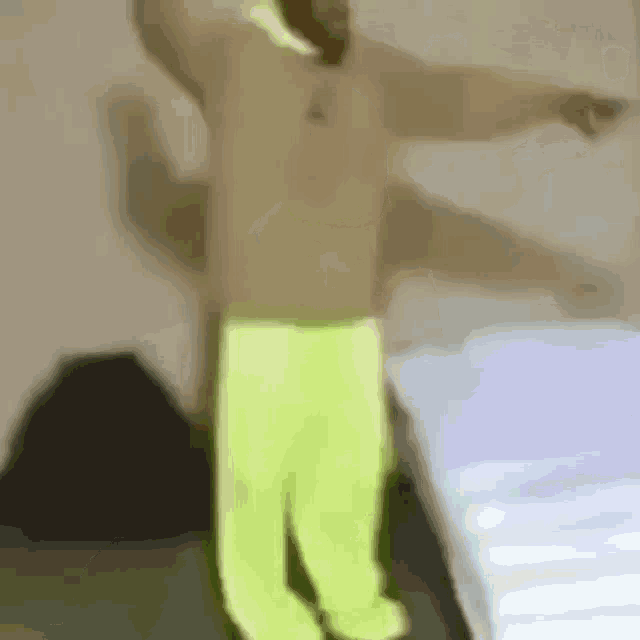 a man in a shirt and neon yellow pants is dancing in a bedroom .