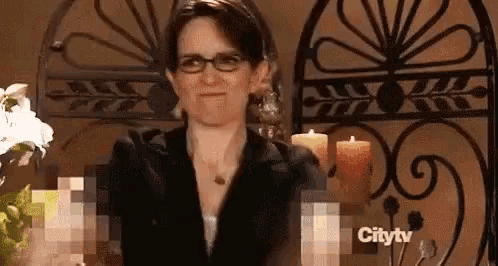a woman wearing glasses is standing in front of candles on a city tv screen