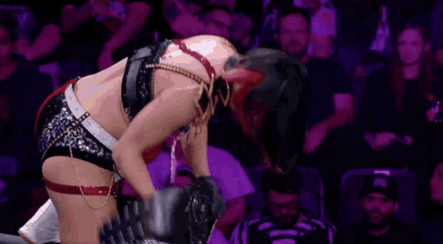 a woman in a wrestling outfit is kneeling down in front of a crowd and a referee .