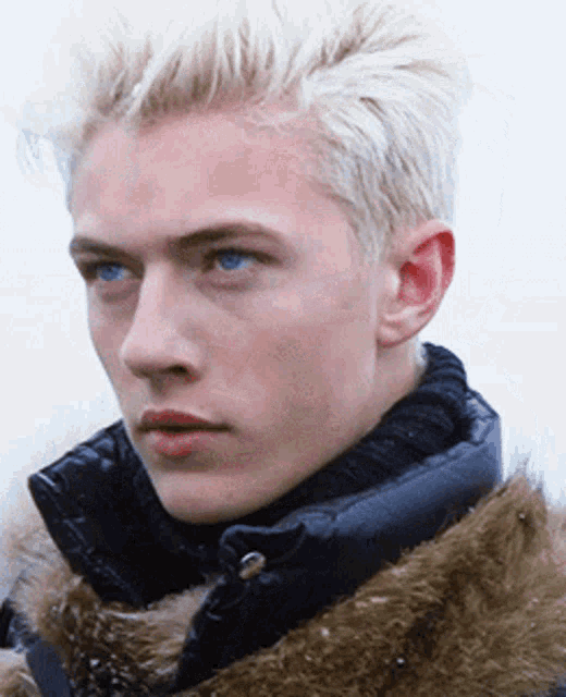 a man with blonde hair and blue eyes wearing a fur coat