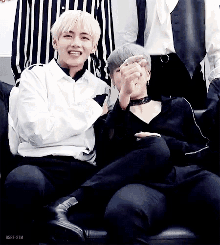 two men are sitting next to each other on a couch and one of them is holding the other 's hand .