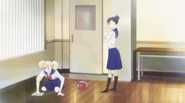 a girl is cleaning the floor while another girl stands behind her with her arms crossed