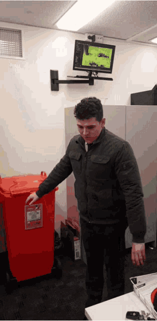 a man in a black jacket is putting something in a red bin