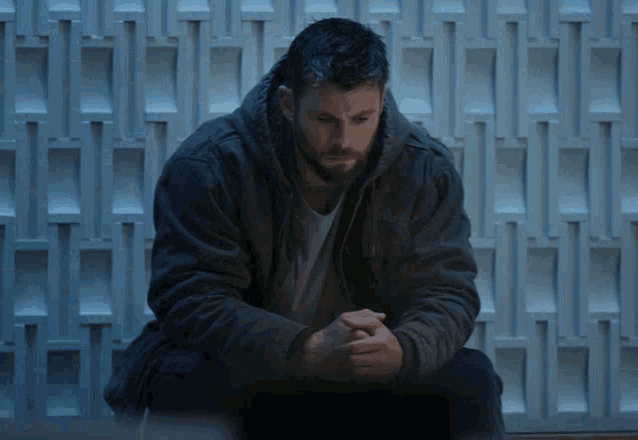 a man with a beard is sitting down with his hands folded