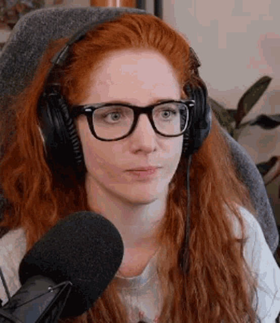 a woman with red hair is wearing headphones and glasses while sitting in front of a microphone .
