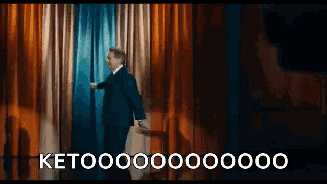 a man in a suit is opening a curtain on a stage and saying ketooo .