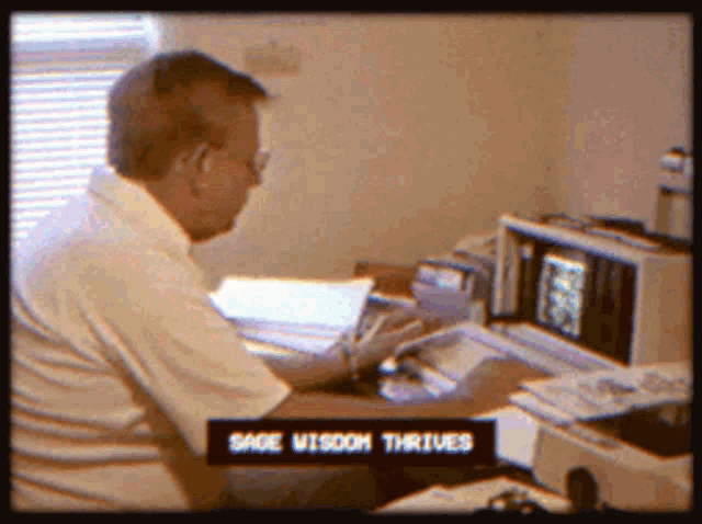 a man sits at a desk with sage wisdom thrives written on the screen behind him