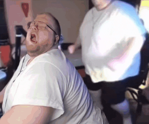 two fat men are dancing in a room and one of them is wearing glasses .