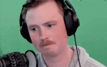 a man wearing headphones and a mustache is laughing in front of a green screen .