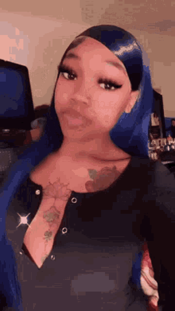a woman with blue hair and a tattoo on her chest is wearing a black shirt .