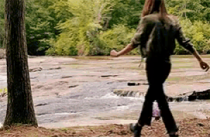 a woman is walking along a river in the woods with a backpack .