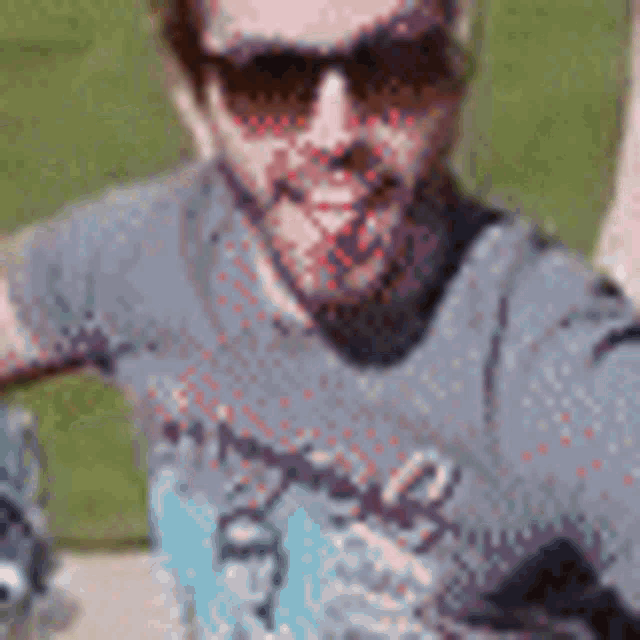 a man wearing sunglasses and a t-shirt is taking a selfie with his hand in the air .