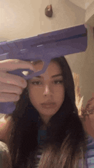 a young woman is holding a purple toy gun over her head .