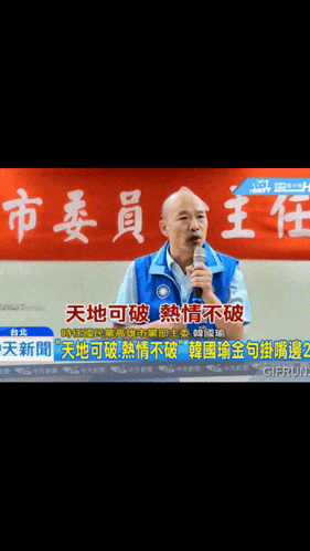 a man in a blue vest is speaking into a microphone with chinese writing behind him