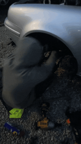 a man is working on a silver car with a dewalt drill