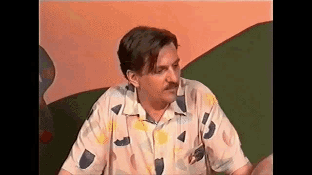 a man in a colorful shirt is sitting on a green couch .