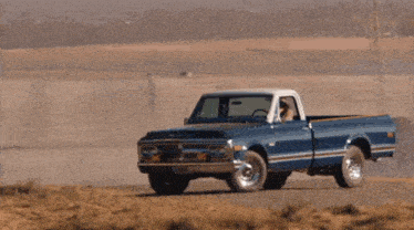 a blue chevrolet truck is driving down a dirt road in the desert