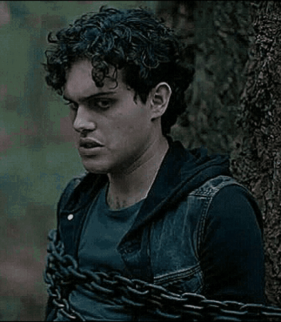 a man with curly hair is chained to a tree trunk