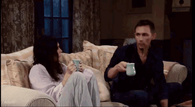 a man and a woman sit on a couch holding cups of coffee
