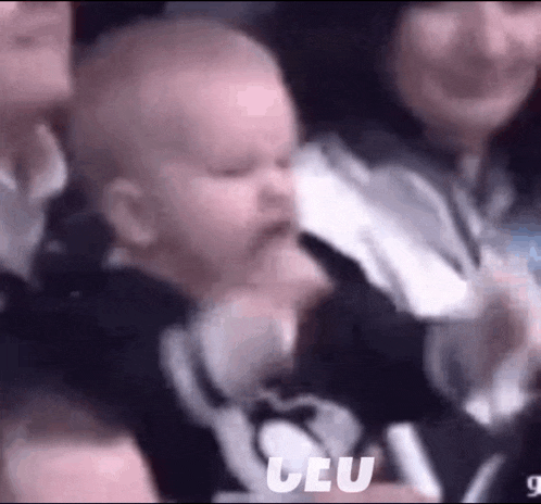 a baby is being held by a woman in a crowd of people and making a funny face .