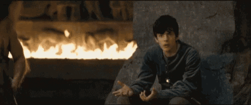 a young man is sitting on a rock in front of a fireplace .