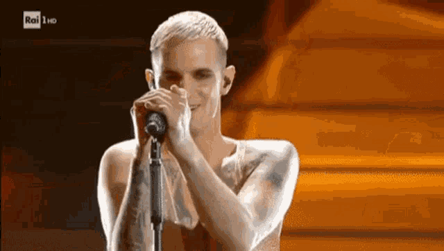 a man without a shirt is singing into a microphone on a stage .