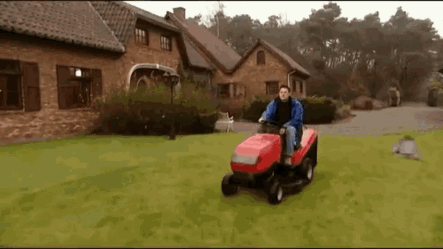 a man is riding a lawn mower on a lush green lawn in front of a house