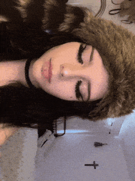 a woman wearing a fur hat and a choker has a cross on the wall behind her
