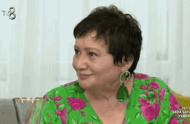 a woman wearing a green and pink floral shirt and earrings is on tv 8