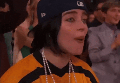 a woman wearing a baseball cap and a yellow and black jersey is sitting in a crowd .